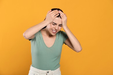 Woman suffering from migraine on yellow background