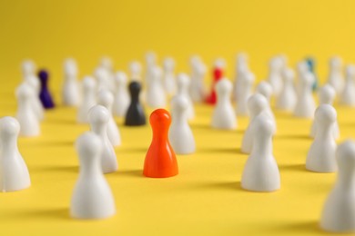 Photo of Colorful pawns on yellow background, closeup. Social inclusion concept