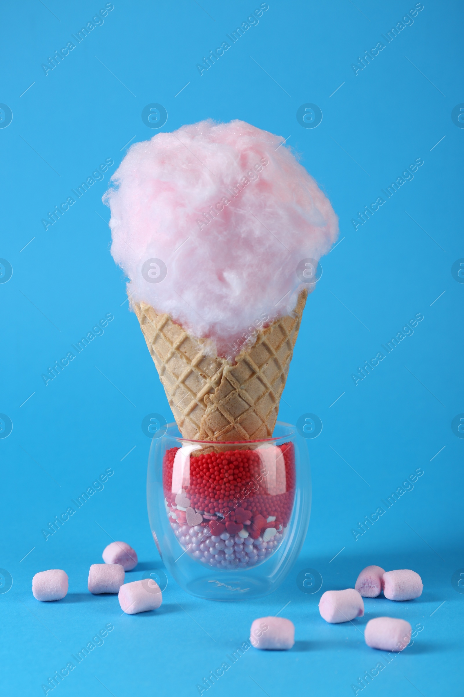 Photo of Sweet cotton candy in waffle cone and marshmallows on light blue background