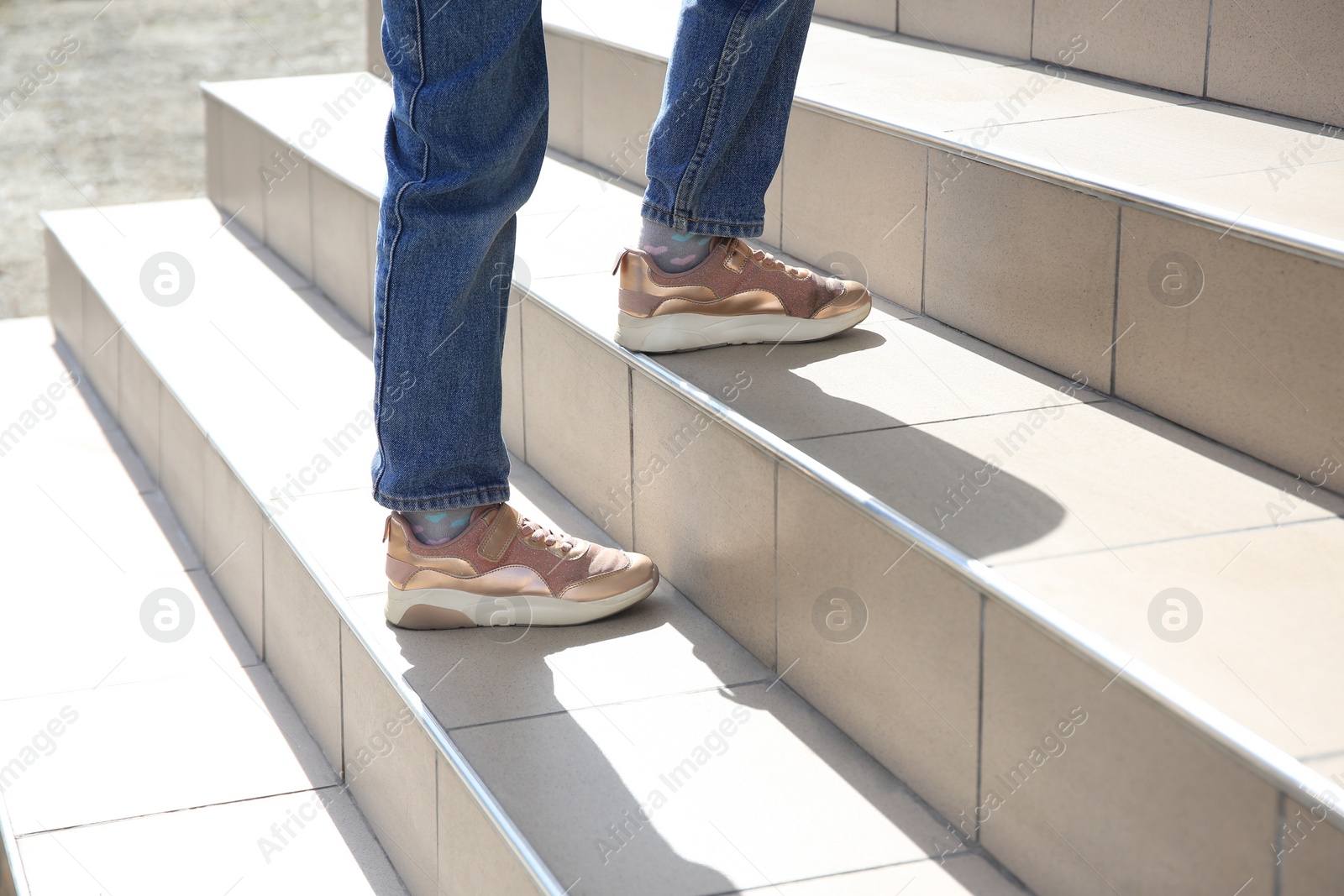 Photo of Woman walking up beige stairs on sunny day, closeup