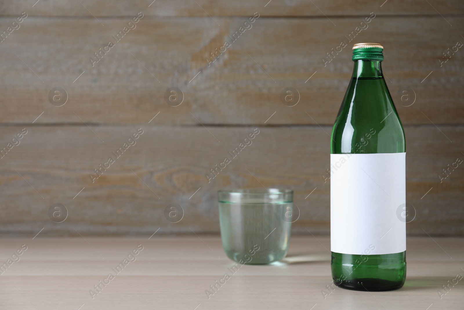 Photo of Bottle and glass with water on wooden table, space for text