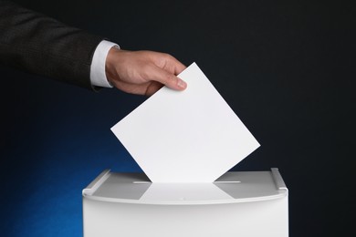 Man putting his vote into ballot box on dark blue background, closeup