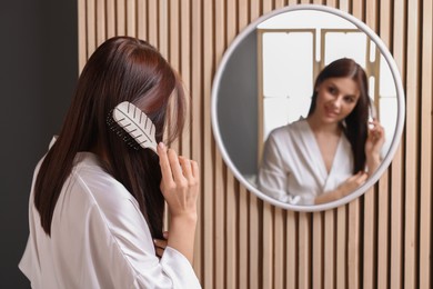 Photo of Beautiful woman brushing her hair near mirror in room, space for text