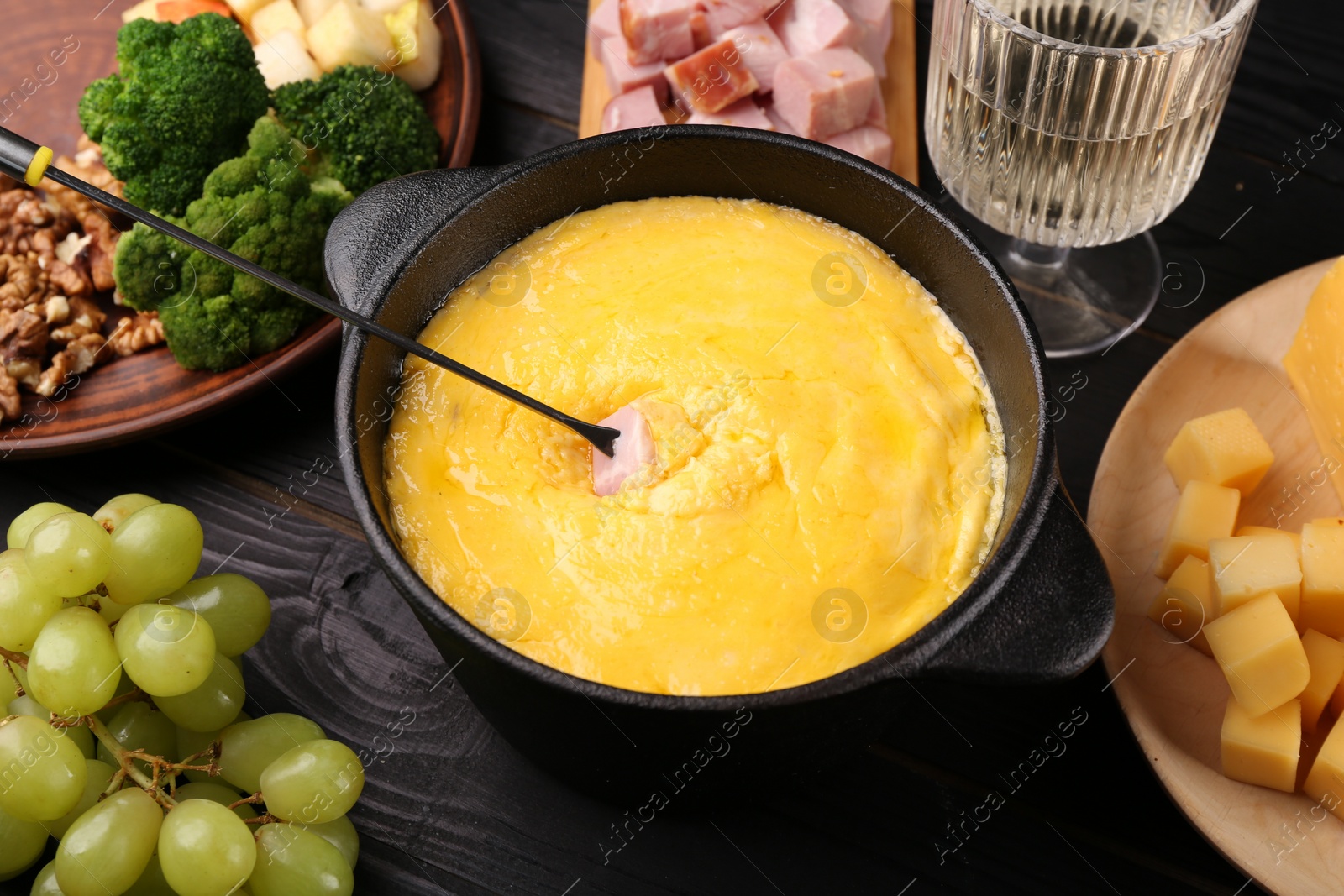 Photo of Fondue pot with melted cheese, fork and different products on black wooden table