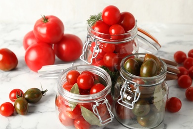 Photo of Pickling jars with fresh ripe tomatoes on white marble table