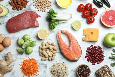 Flat lay composition with fresh meat and other products for balanced diet on white marble table