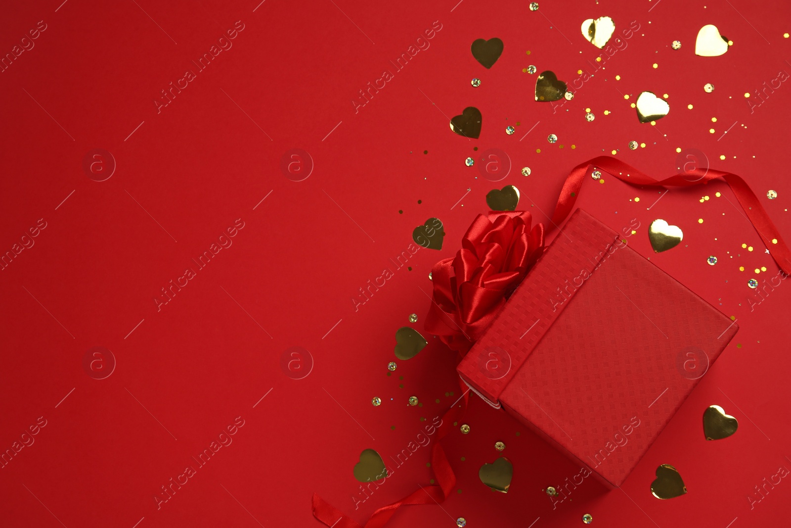 Photo of Gift box and shiny confetti on red background, top view. Space for text