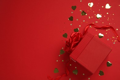 Photo of Gift box and shiny confetti on red background, top view. Space for text