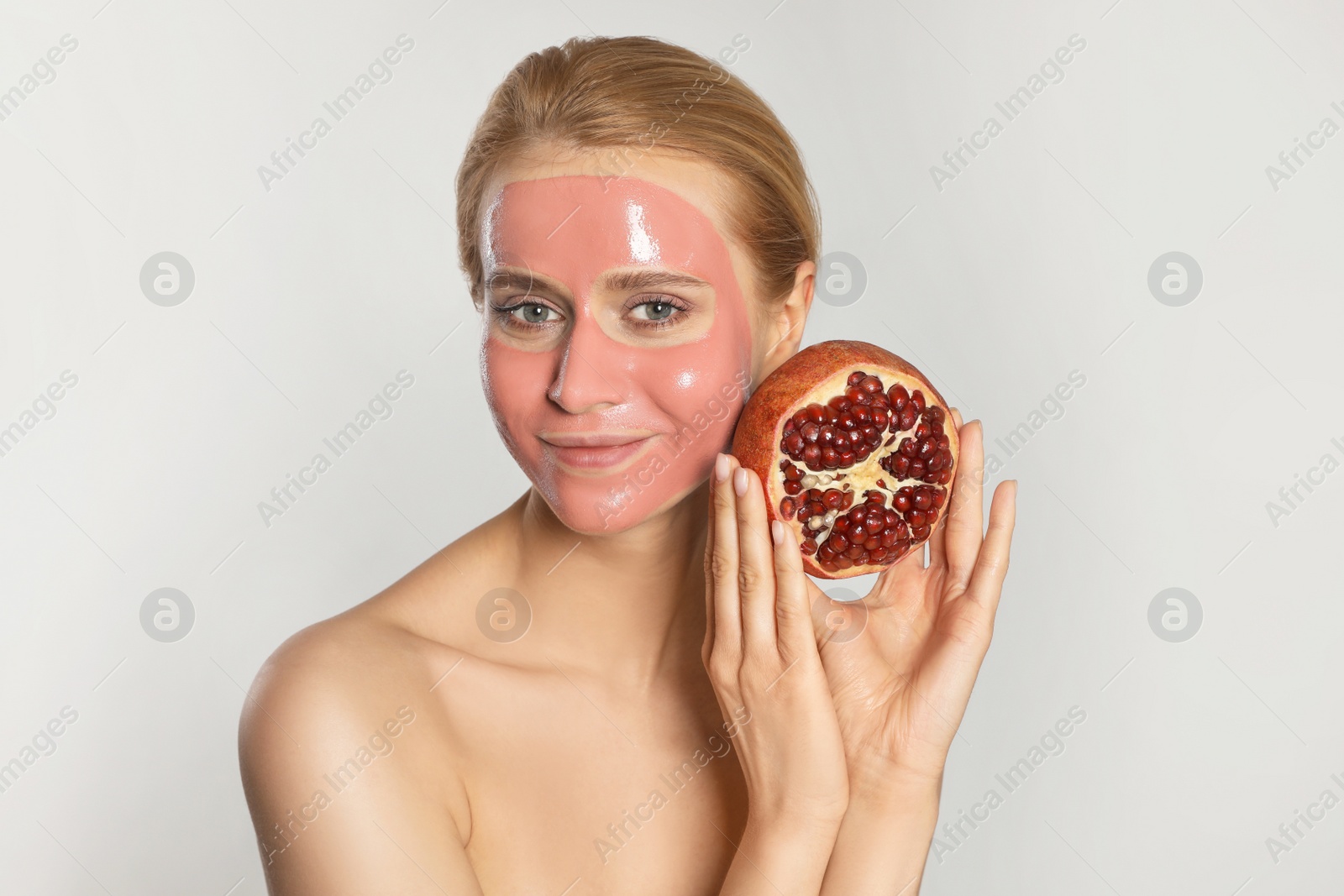 Photo of Young woman with pomegranate face mask and fresh fruit on light grey background