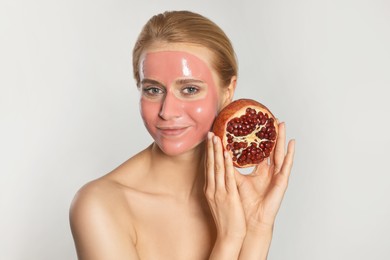 Young woman with pomegranate face mask and fresh fruit on light grey background