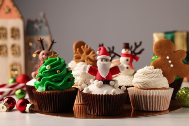 Photo of Different beautiful Christmas cupcakes and baubles on white table