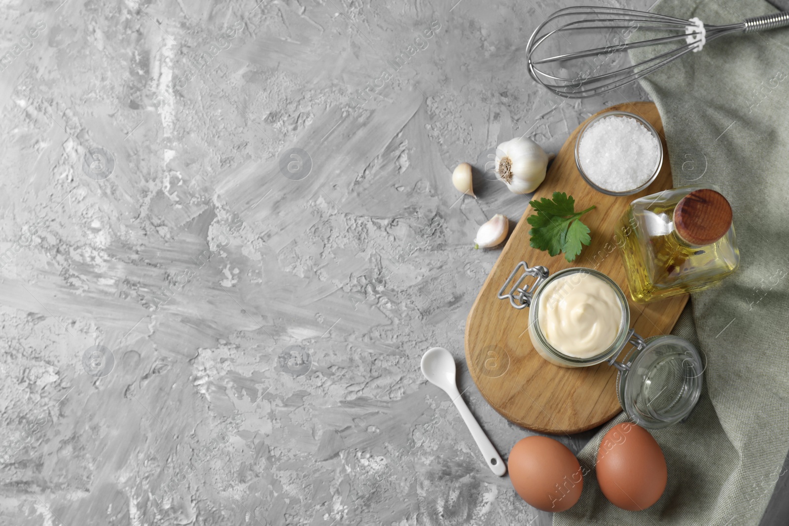 Photo of Tasty mayonnaise in jar, ingredients and whisk on gray textured table, flat lay. Space for text