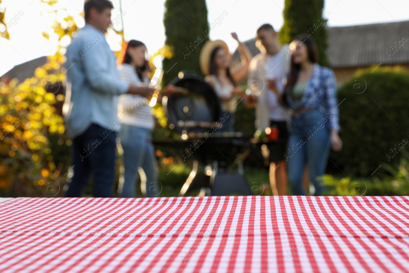 Photo of Empty table and blurred view of friends having barbecue party outdoors. Space for text