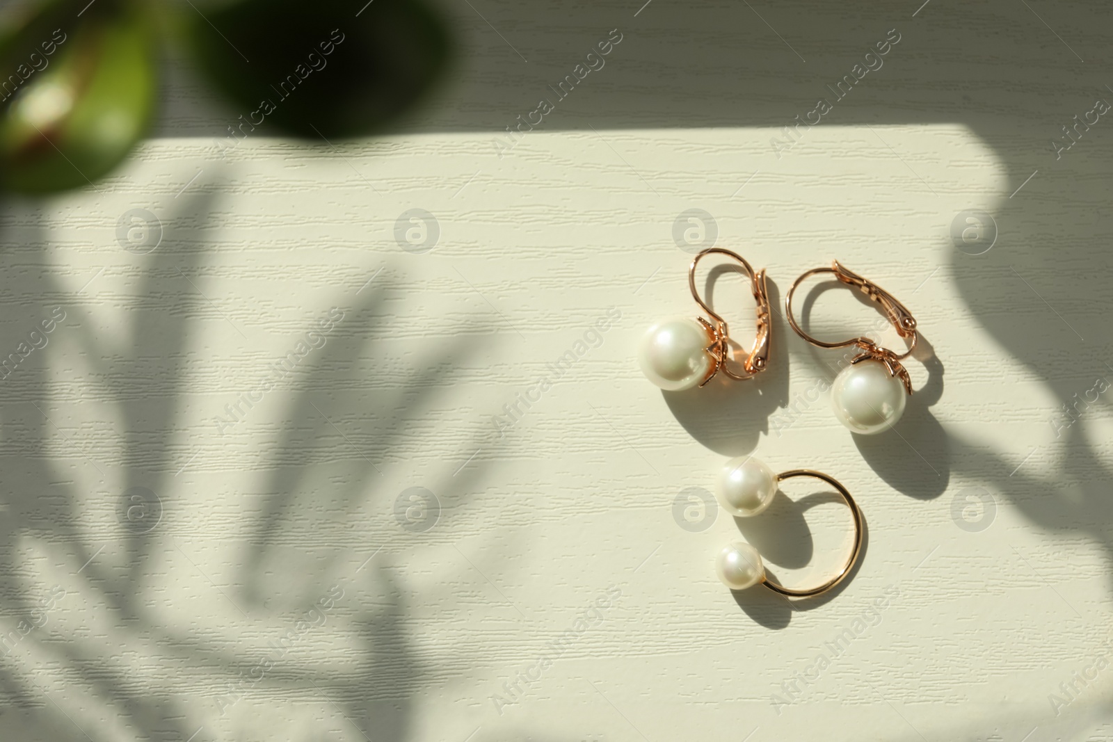 Photo of Elegant golden ring and earrings with pearls on white wooden table, flat lay. Space for text