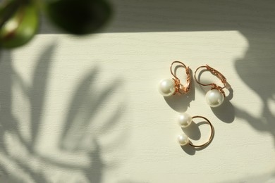 Elegant golden ring and earrings with pearls on white wooden table, flat lay. Space for text