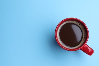 Photo of Red mug of freshly brewed hot coffee on light blue background, top view. Space for text