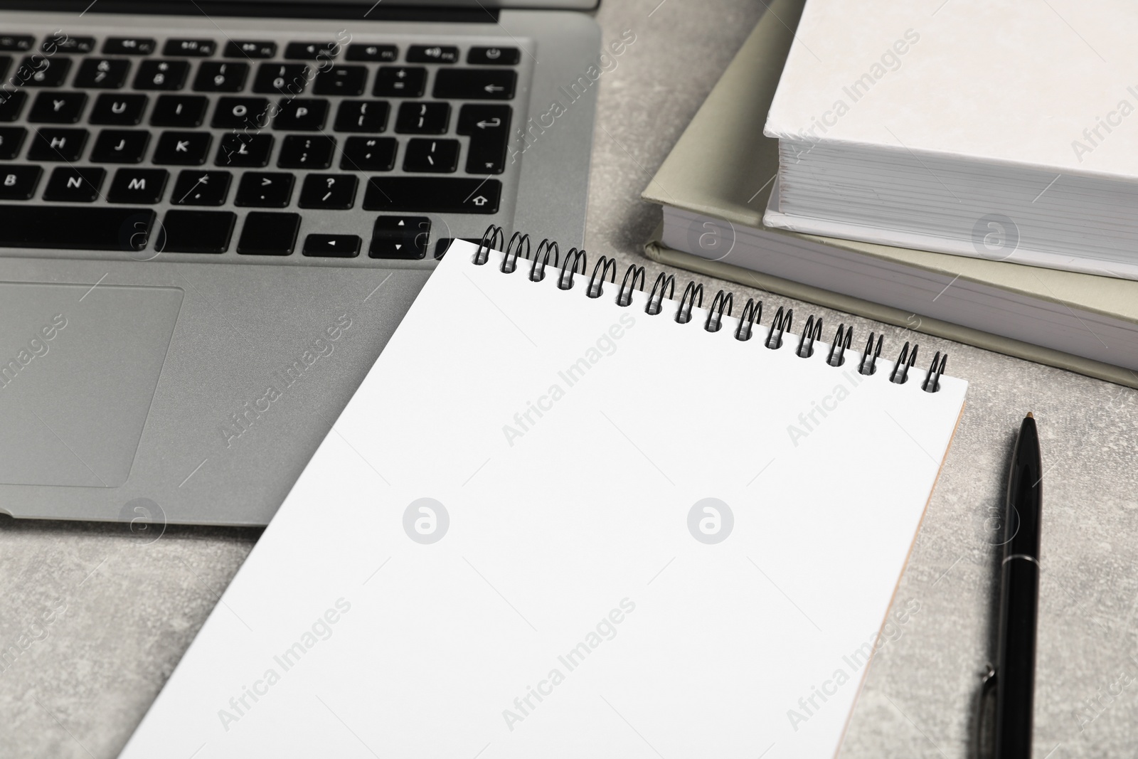 Photo of Empty notebook, laptop, books and pen on light grey table