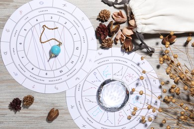 Photo of Astrology prediction. Zodiac wheels, pendulum, gemstone and pouch with dry flowers on wooden table, flat lay