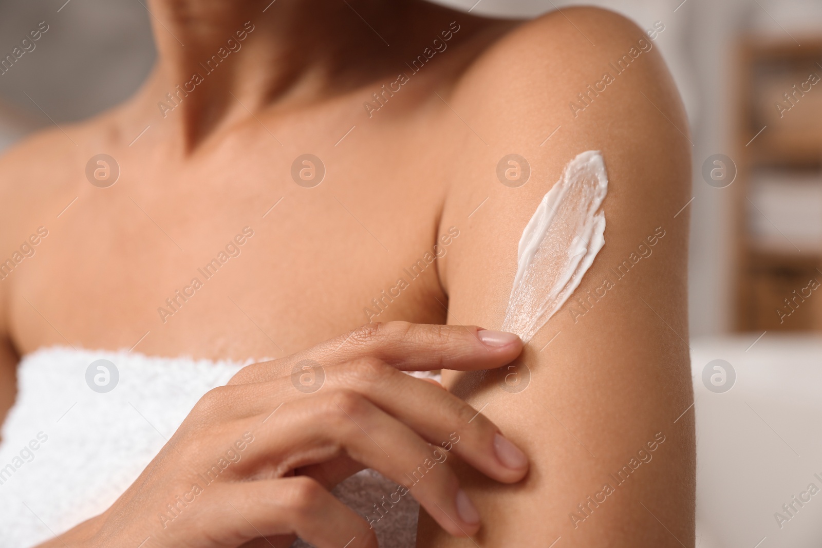 Photo of Woman applying body cream onto arm indoors, closeup