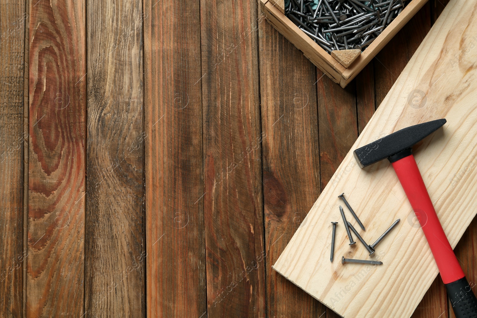 Photo of Hammer, metal nails, plank and crate on wooden table, flat lay. Space for text