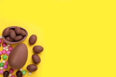 Photo of Delicious chocolate eggs and candies on yellow background, flat lay. Space for text