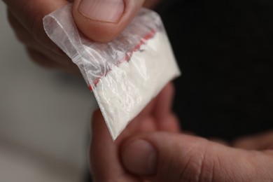 Drug addiction. Man with plastic bag of cocaine on light background, closeup