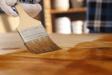 Photo of Man with brush applying wood stain onto wooden surface indoors, closeup