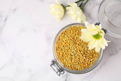 Photo of Fresh bee pollen granules in jar and flowers on light table, top view. Space for text
