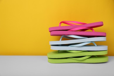 Photo of Stack of different flip flops on white table against yellow background, space for text
