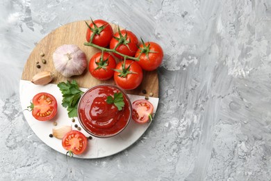 Photo of Delicious ketchup in bowl, parsley, garlic and tomatoes on grey textured table, top view. Space for text