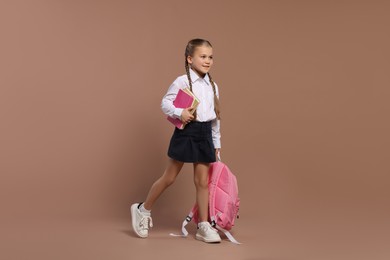 Happy schoolgirl with backpack and books on brown background