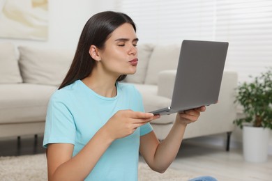 Photo of Young woman having video chat via laptop and sending air kiss at home
