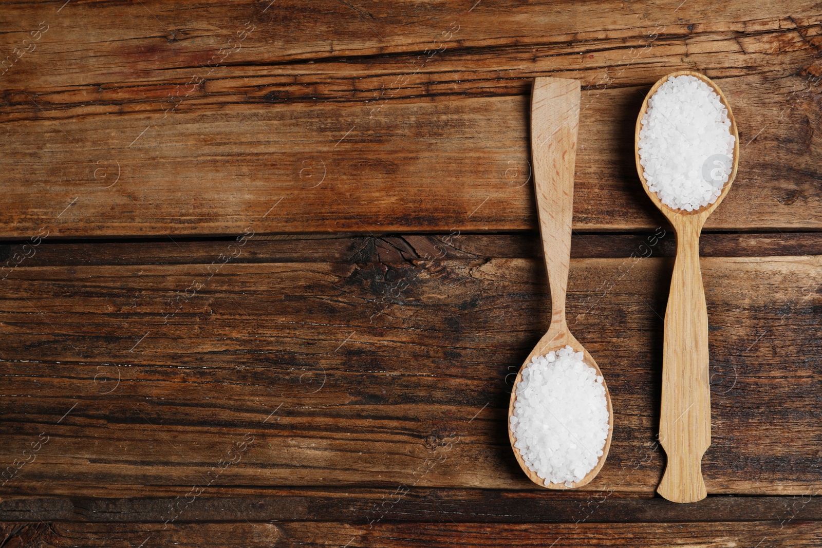 Photo of Spoons with natural sea salt on wooden table, flat lay. Space for text