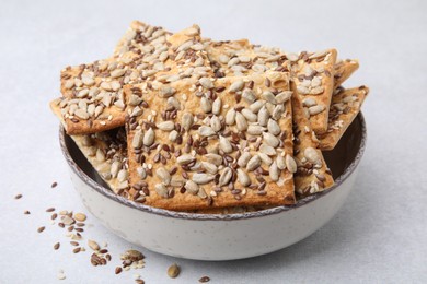 Photo of Cereal crackers with flax, sunflower and sesame seeds in bowl on light textured table, closeup