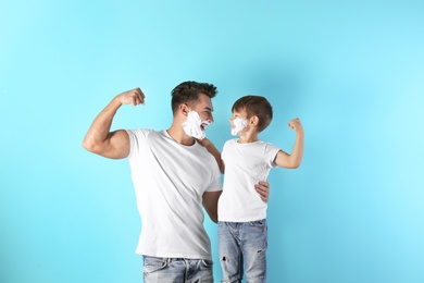 Photo of Father and son with shaving foam on faces against color background