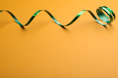 Photo of Shiny green serpentine streamer on orange background. Space for text