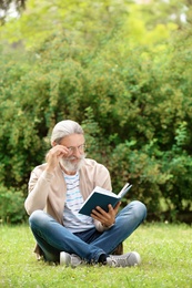 Photo of Handsome mature man reading book on green grass in park