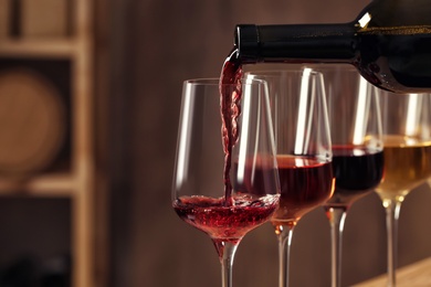 Photo of Pouring wine from bottle into glass in cellar, closeup