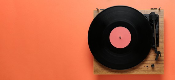 Photo of Modern turntable with vinyl record on coral background, top view