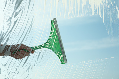 Photo of Woman cleaning window with squeegee on spring day, closeup