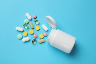 Photo of White bottle and different vitamin pills on light blue background, top view