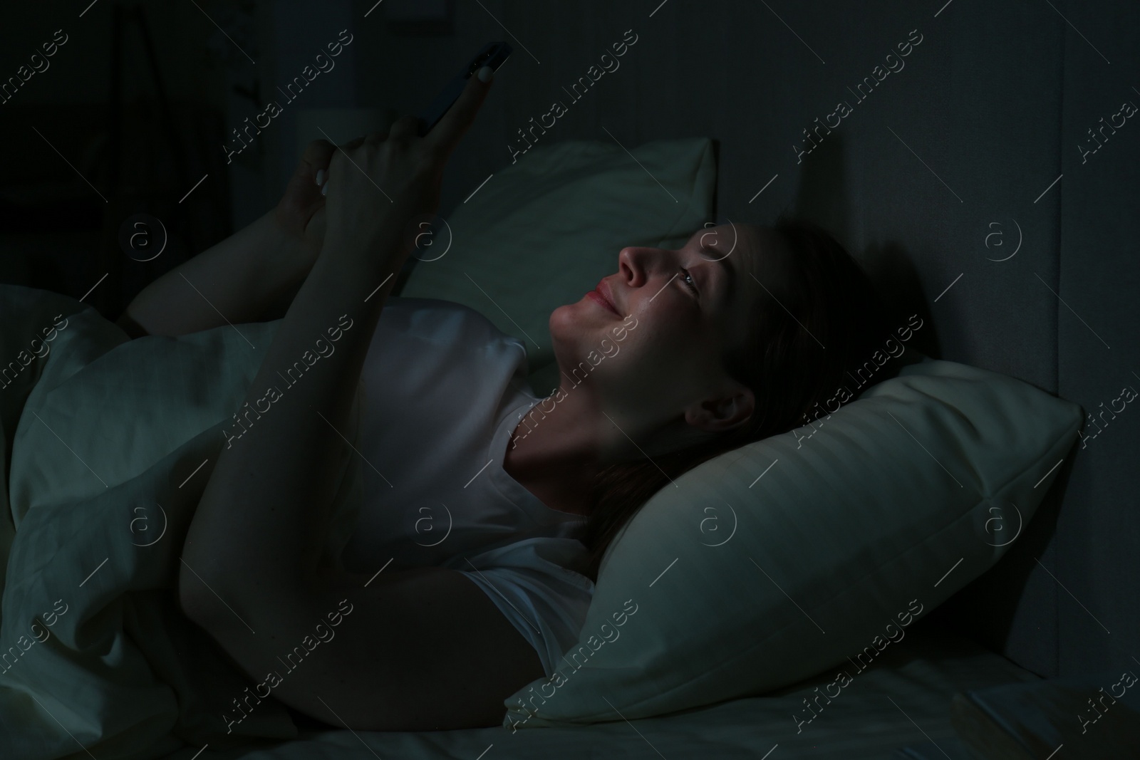 Photo of Woman using smartphone on bed at night. Internet addiction