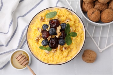 Photo of Tasty cornmeal with blueberries, dates, walnuts and honey in bowl on white table, flat lay