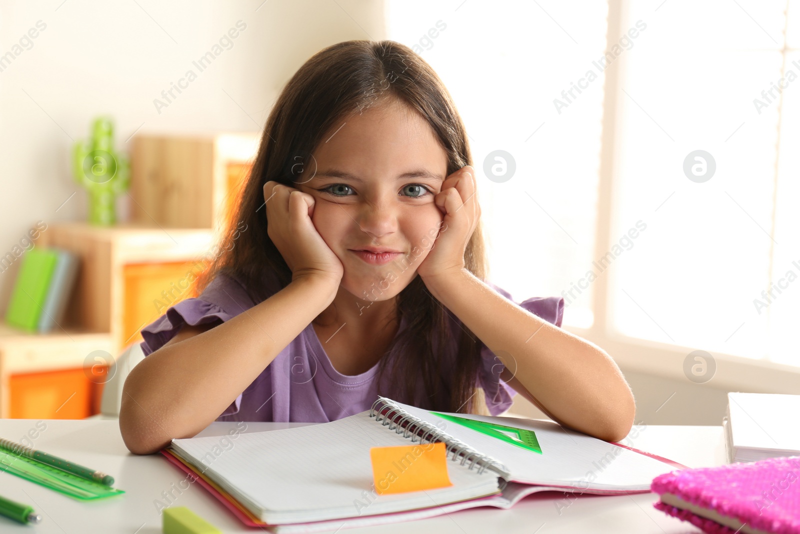 Photo of Emotional little girl doing homework at table indoors