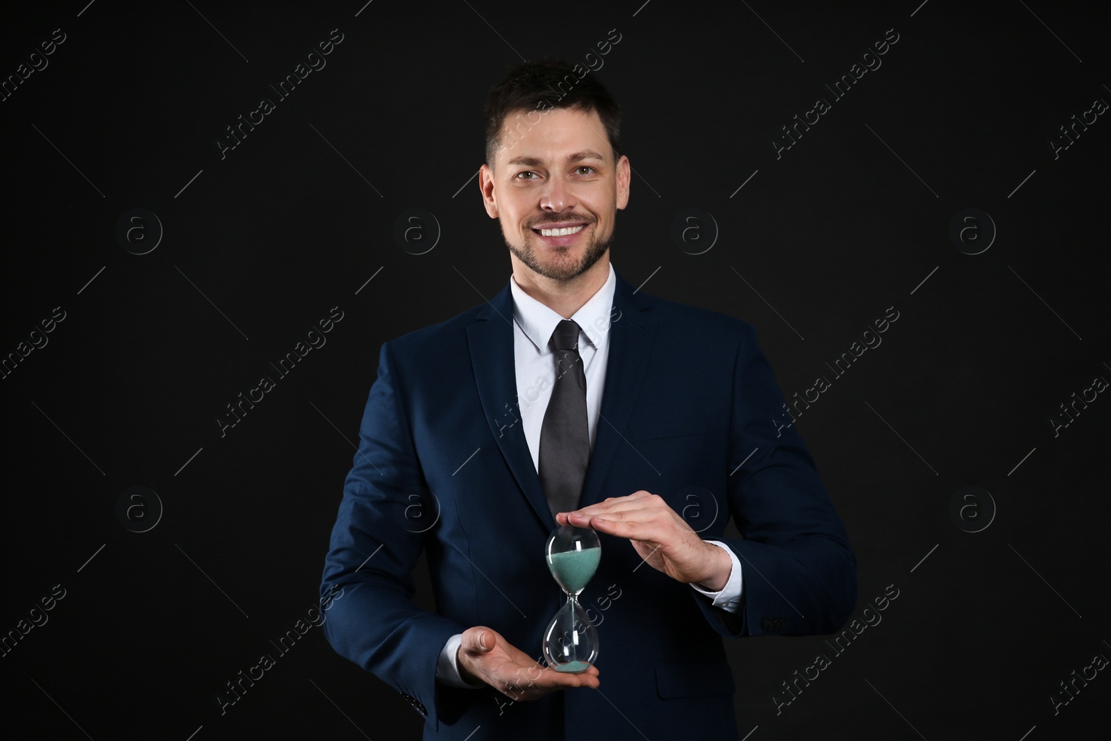 Photo of Happy businessman holding hourglass on black background. Time management