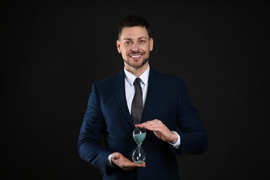 Photo of Happy businessman holding hourglass on black background. Time management