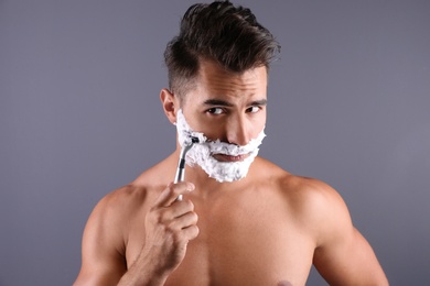 Handsome young man shaving on color background