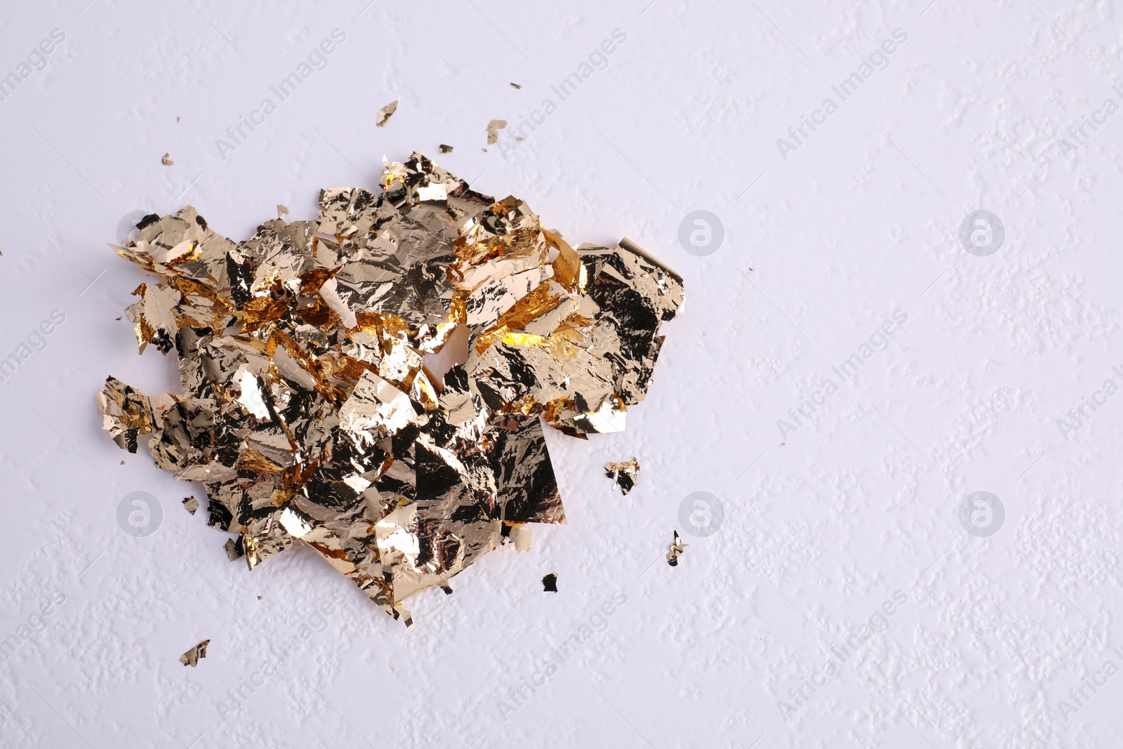 Photo of Many pieces of edible gold leaf on white textured table. Space for text