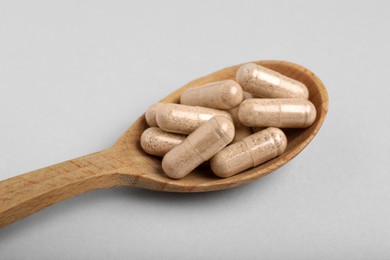 Photo of Gelatin capsules in spoon on light grey background, closeup