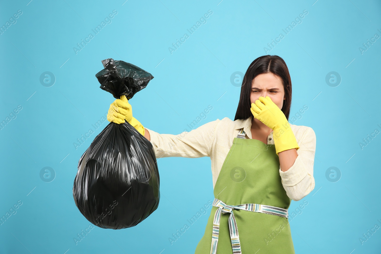 Photo of Woman holding full garbage bag on light blue background